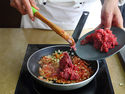 大煎锅里煸炒红洋葱和大蒜;加入牛肉麋炒至变色。